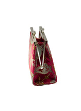 A small clutch purse with a pink and gold floral brocade fabric exterior, featuring a silver-tone metal kiss-lock closure, shown on a neutral light gray background.