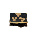 A small rectangular black fabric case with gold trim and a pattern of beige circular motifs on the lid, shown open on a light gray background.