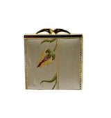 A small rectangular clutch purse with a gold-tone metal frame and bow clasp, featuring a silver-gray satin body with an embroidered floral motif in green, yellow, and red.