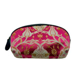 A small zippered cosmetic pouch with a vibrant pink and gold brocade pattern, featuring a black zipper and a small black tassel pull on the left side, set against a plain white background.
