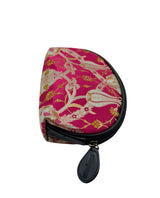 A small semicircular zip pouch with a vibrant pink and gold patterned fabric exterior, black zipper, and a black leather pull tab on a light gray background.